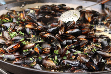 Mussels with parsley and sauce in a large frying pan. Food court. Street food. Mussels with shells cooked with herbs in a frying pan. Mussels cooked in sauce at a street market. Cooking a seafood dish