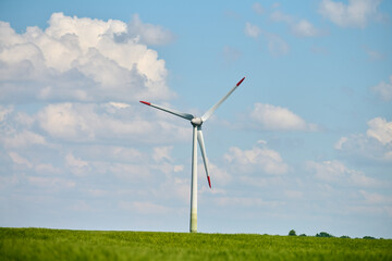 Wind turbine stands tall in lush green wheat field beneath bright blue sky with fluffy white clouds...