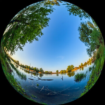 Fisheye view of river bank with tree. A river in a non-urban area with picturesque nature. Countryside landscape on summer day. Fulldome HDR format photo for planetarium, taken through a circular lens
