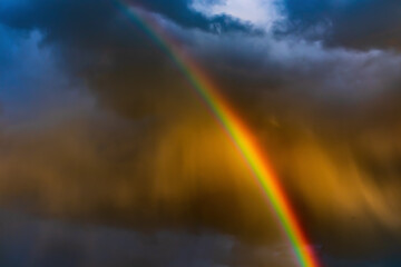 A bright rainbow in the sky in dark rain clouds. A rainbow is an optical phenomenon caused by...