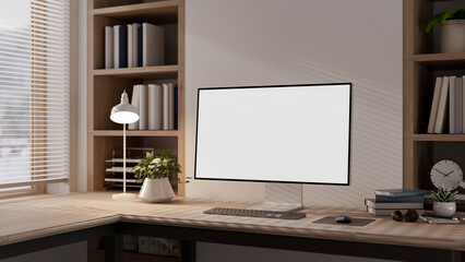 Blank screen computer with a lamp and books on wooden table in a room with a blind covered window.