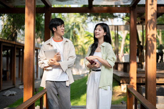 Smiling asian man is talking to his female friend and standing together in gerden wooden corridor.