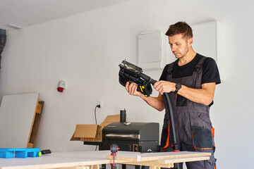 Worker in workwear attaching vacuum hose to electric jigsaw for woodworking on workbench in home workshop © Lazy_Bear