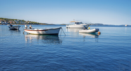 Several small boats floating peacefully on calm, clear blue sea waters with a distant coastal...