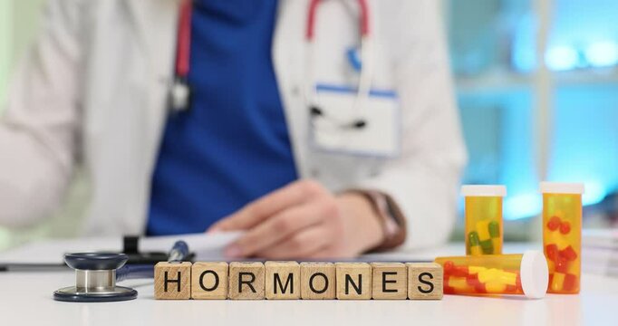 Text Hormone of wooden cubes with stethoscope and pills against doctor. Female medic stamps prescription for therapy in hospital office slow motion
