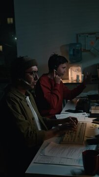 Medium vertical shot of pushy, aggressive male scam call center worker sitting at computer in office, engaged in conversation with victim, gesticulating, pressuring them into revealing passcode