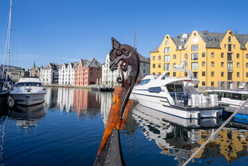 Viking figurehead of a ship prow ornament docked in the Brosundet canal, with colorful Art Nouveau buildings of Alesund, Norway reflected in a sunny day