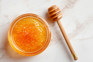 Fototapeta premium A golden honey face mask in a small glass bowl, placed on a white marble background with a honey dipper and a soft brush, viewed from above, evoking a rich and nourishing spa moment