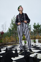 A Stylish Individual Wearing Striped Pants Poses at an Outdoor Chess Board Under the Sun