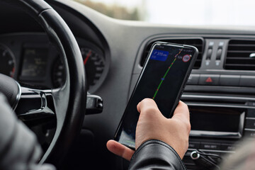 Driver in a black leather jacket checks a navigation app on a smartphone while driving, emphasizing...