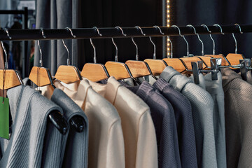 Row of cozy knit sweaters in soft neutral colors on wooden hangers creates a sense of warmth and comfort in a stylish modern boutique.
