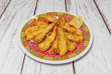A plate full of tempura prawns with a slice of fresh lemon