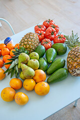 A table full of tomatoes, avocados, and other fresh fruits, such as pineapples and tangerines on a light blue metal table