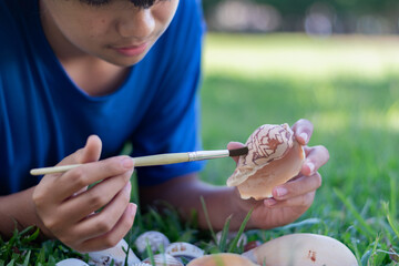 A young boy carefully cleans a seashell with a brush while lying on the grass, showcasing...
