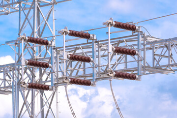 Insulators on high voltage electric pylon structure in power distribution substation against blue sky background