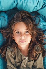 A girl with long brown hair is laying on a blue blanket