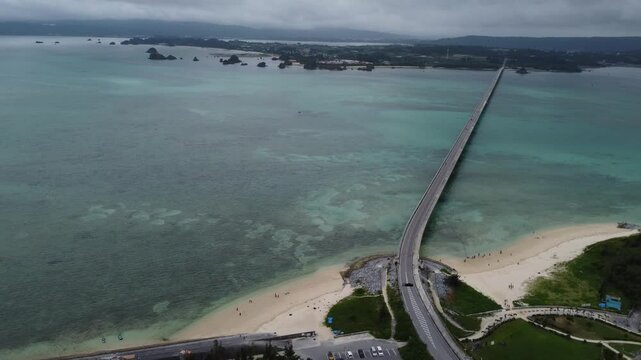4K focus on road over Long bridge of Kouri Island and beach from a high view by drone with clear sky and sea water.