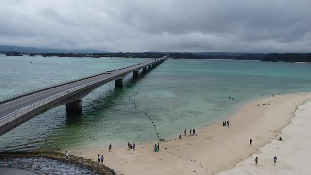 4K focus on road over Long bridge of Kouri Island and beach from a high view by drone with clear sky and sea water.