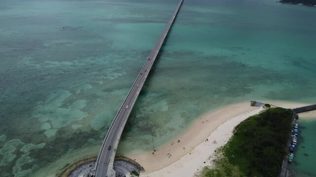 4K focus on road over Long bridge of Kouri Island and beach from a high view by drone with clear sky and sea water.