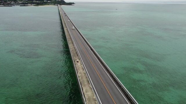 4K focus on road over Long bridge of Kouri Island and beach from a high view by drone with clear sky and sea water.