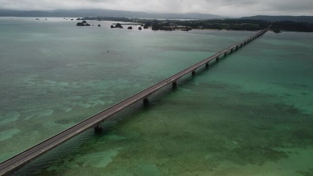4K focus on road over Long bridge of Kouri Island and beach from a high view by drone with clear sky and sea water.