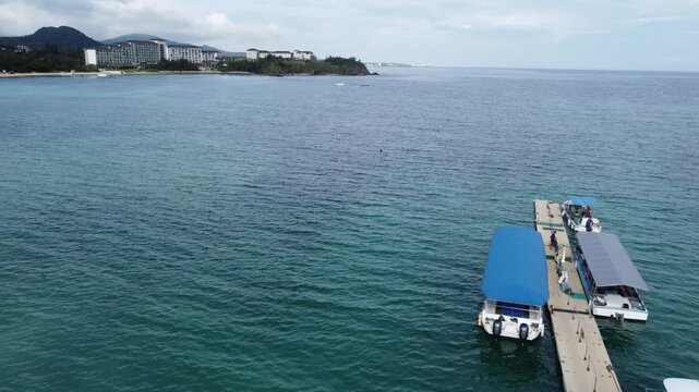 4K over the serene seascape of Okinawa showcases crystal-clear waters, exposed rocky formations, and gentle waves lapping against the shore