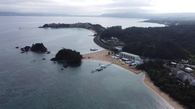 4K over the serene seascape of Okinawa showcases crystal-clear waters, exposed rocky formations, and gentle waves lapping against the shore