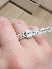 Hand holding measuring tape for ring size measurement on finger.