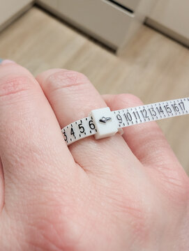 Hand holding measuring tape for ring size measurement on finger.
