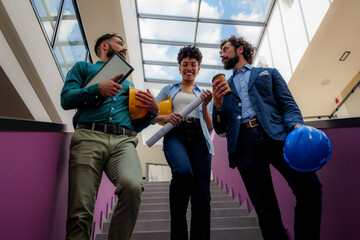 Group of architects and engineers are walking down the stairs in a modern office building, holding blueprints, hardhats and takeaway coffee, discussing a project © DusanJelicic