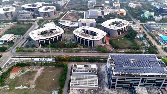 An expansive aerial shot captures a sprawling, modern technology park or corporate campus bathed in the warm glow of a setting or rising sun. The sky is hazy