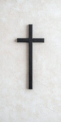simple black wooden christian cross mounted on textured white plaster wall, symbolizing faith, reverence, and spiritual belief