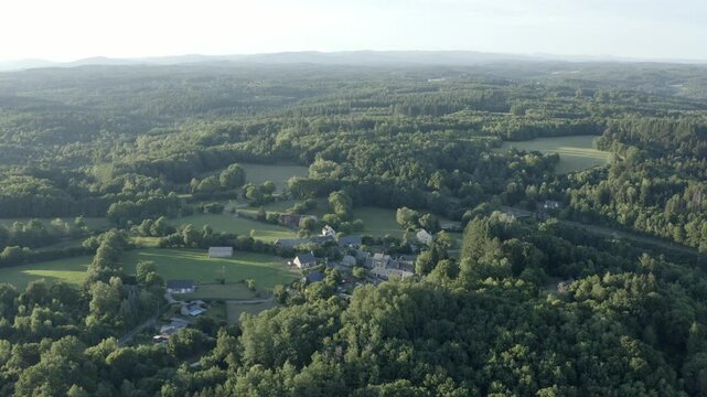 Aerial view of vast green forest landscape with small village nestled among trees, hazy horizon, Marcillac La Croisille, France