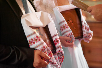 Bride and groom holding religious icons wrapped in traditional embroidered cloth during Orthodox...