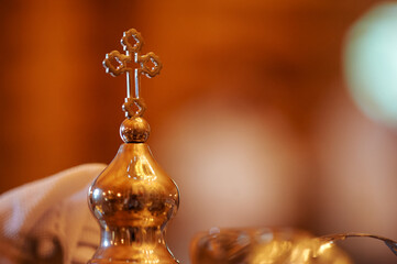 Golden Christian cross atop ceremonial vessel in church setting with warm blurred background.