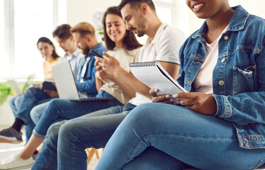 Cheerful multiracial young people in casual clothes sitting in row studying together indoors. Happy students group preparing for test with laptops and mobile phones. Education and people concept. © Studio Romantic