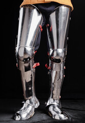 Detailed view of reflective medieval leg armor with intricate design and historical relevance. The...