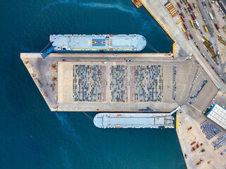 Aerial top down view of an industrial car port terminal with a cargo ship unloading and rows of new vehicles for delivery