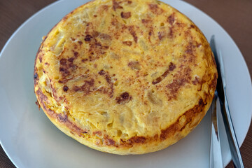 Homemade whole tortilla set on a table, golden-brown omelette prepared with eggs, thinly sliced potatoes and sweet onions showing the rich texture and rustic appeal of this traditional Spanish dish