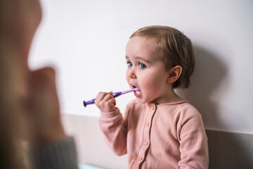 A cute toddler is brushing their teeth with a purple toothbrush. This young child practices good dental hygiene habits in the bathroom during their daily routine.