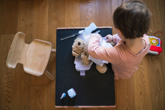 Young child plays with a teddy bear, changing its diaper on a small table. This imaginative play helps children learn and develop skills at home.