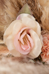 Delicate artificial rose in soft cream and blush pink tones, surrounded by beige pampas grass and other fabric flowers and decor, pastel arrangement resembling natural feminine curves and textures