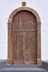 Alte braune Kirchentür aus Holz in einem runden Steinportal und weißer Fassade