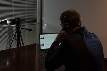 An undercover agent works at night: camera, headphones, audio recording on a laptop screen.