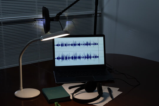 Set up listening and audio recording: a laptop with audio wave display, directional microphone, headphones and writing materials on the table. The concept of surveillance, podcasting,