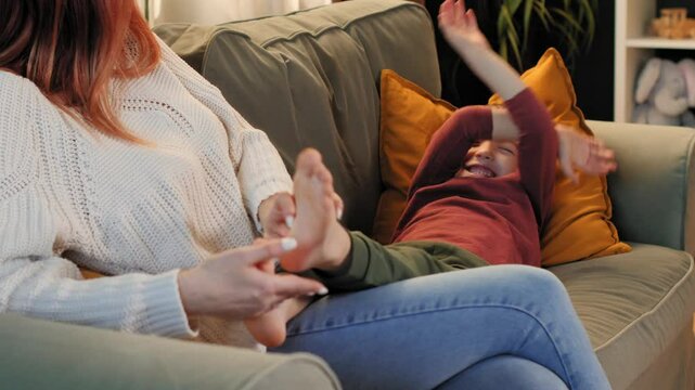 Mother and son tickling and laughing on sofa at home