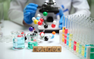 This image shows a closeup of sulfur research with a microscope and colorful test tubes in a lab setting