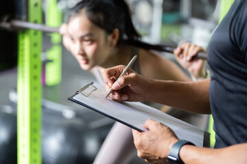 Fitness Assessment. Trainer recording performance of young woman during squat exercise.