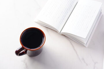 テーブルの上の開いた本とコーヒーカップで、コーヒーを飲みながら読書を楽しんでいるイメージ
