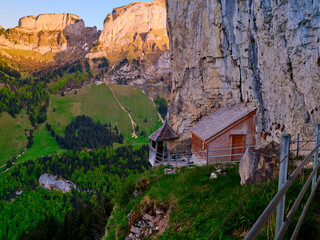 Scenic mountain view featuring a rustic cabin nestled against a cliff in the Swiss Alps during sunset